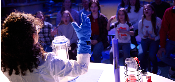 A Science Center staff member performs a demonstration for an audience.