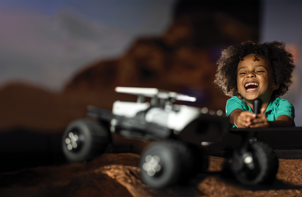 Child laughing and using a joystick to operate a Mars rover.