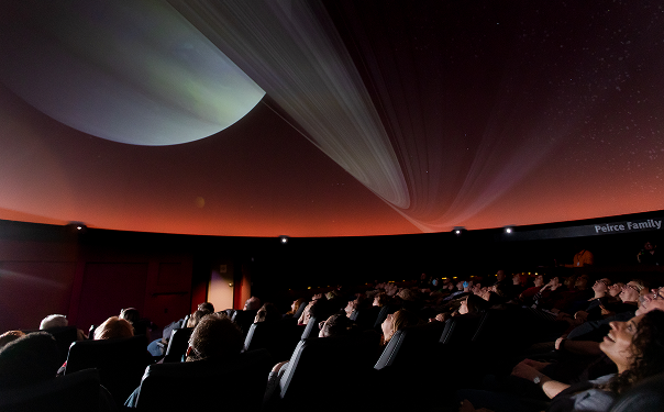 Audience in Buhl Planetarium watching a projection of a planet on a large dome screen.