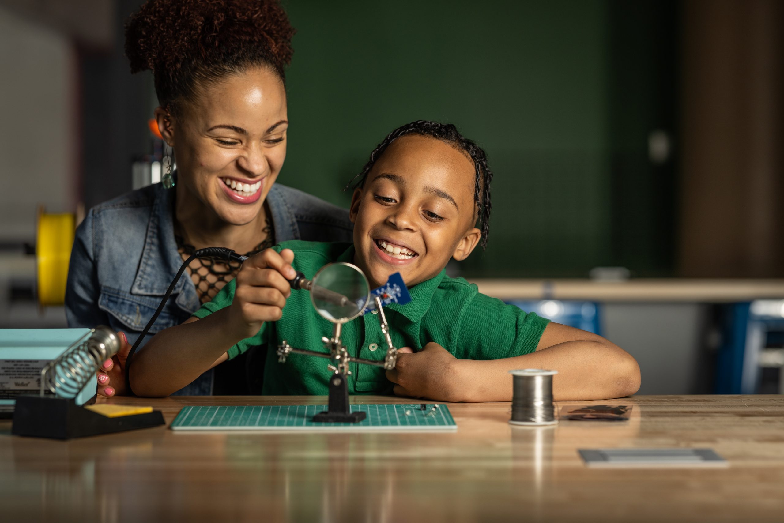 A mother smiles as her young son is soldering in BNY Fab Lab