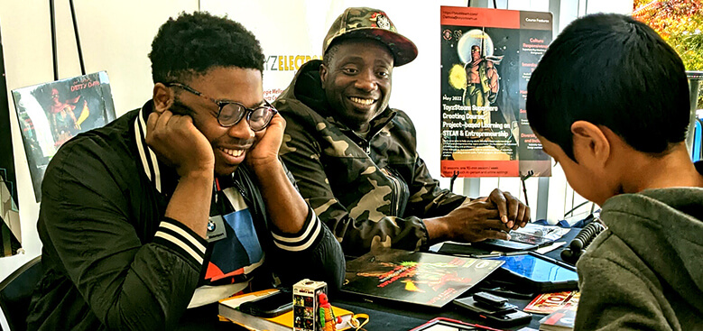 Superhero creators at a table showing projects to a boy