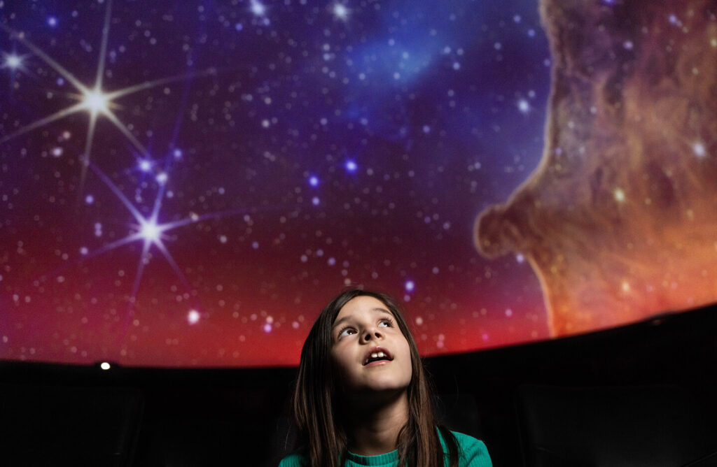 A young girl looking up at a colorful, starry sky in a planetarium.