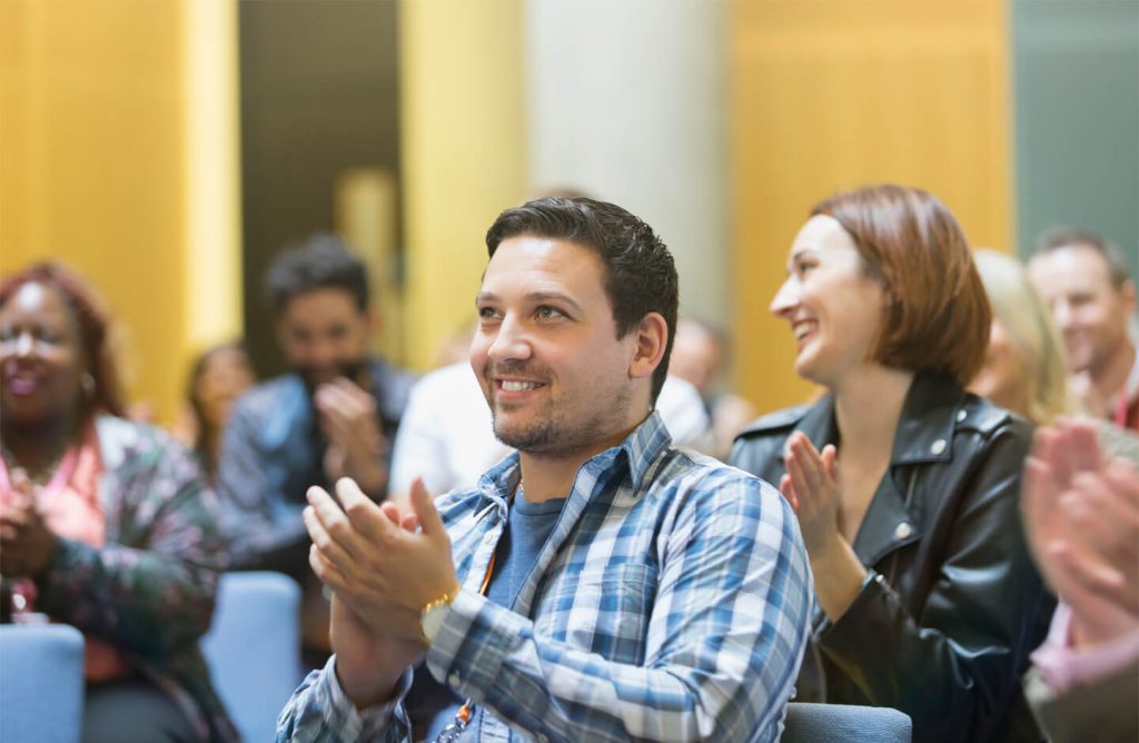 An adult audience seated and clapping