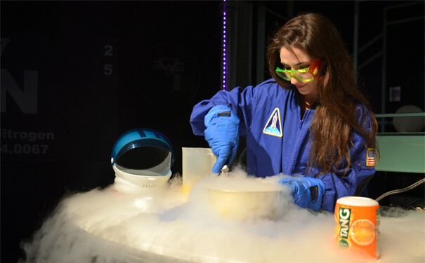 Staff educator wearing protective glasses and gloves, wearing an astronaut suit, and scooping liquid nitrogen