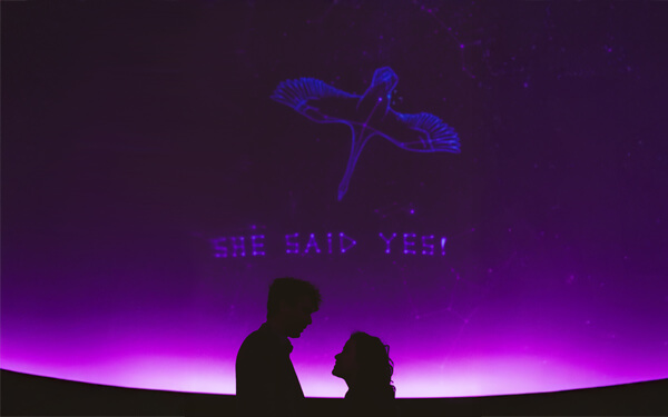 A couple in Buhl Planetarium with lasers showing the words - She said yes -