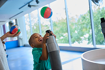 A child playing with a hose that is blowing air on a ball to make it float