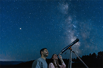 A young man and woman outside at looking through a telescope at the night sky.
